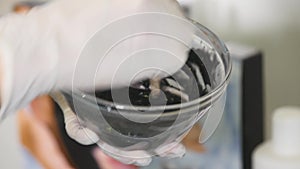 Cosmetologist squeezes cream from a tube on a glass saucer. Hands in medecine gloves