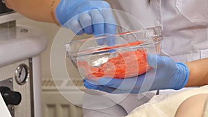 Cosmetologist squeezes cream from a tube on a glass saucer. Hands in medecine gloves