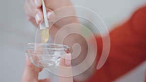 cosmetologist squeezing cosmetic serum from pack to glass bowl in beauty salon, closeup