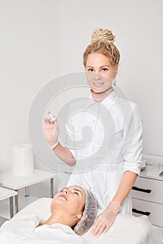 Cosmetologist with syringe prepares to make rejuvenation injection in woman face skin in salon