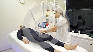 A cosmetologist-therapist gives a man in a special black suit an anti-cellulite LPG massage in a beauty salon. A doctor