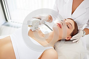 Cosmetologist treating neck, decollete area and chest of woman with laser machine photo