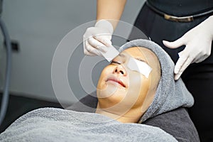 Cosmetologist use a cotton pad to prepare receiving skin gel and color light therapy to stimulate facial health on woman client