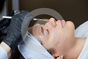 Cosmetologist uses a brush to apply a superficial face peeling to a woman