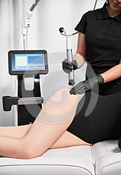 Beautician performing radiofrequency treatment on woman hip. photo