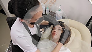 A cosmetologist wipes the eyebrows with cotton swabs after a permanent makeup.