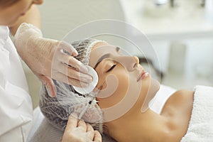 Cosmetologist wiping skin with cotton pads during facial beauty botox injection for young womans cheek