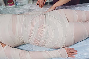 The cosmetologist wraps the leg of the customer. Anti-cellulite procedure-STYX wrap.