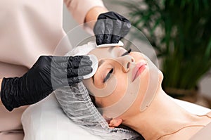 Cosmetologists doing facial massage and professional skin cleaning. Beautiful woman in spa salon getting face treatment