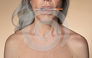 Cosmetology for aged women. European senior woman holding syringe with hyaluronic acid for lip augmentation in her mouth