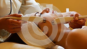 Cosmetology. Beautiful Woman At Spa Clinic Receiving Stimulating Electric Facial Treatment From Therapist. Closeup Of