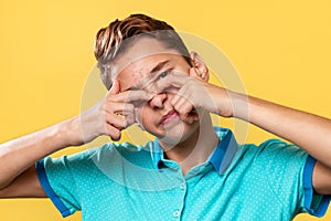 Cosmetology, Dermatology and acne. Caucasian teenager in a blue t-shirt, painfully squeezes out a pimple on his nose. Yellow