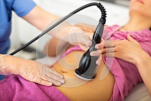 Cosmetology doctor makes a young female client a vacuum massage of the abdomen