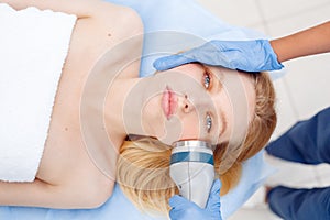 Cosmetology Service. Young woman at beauty clinic lying while doctor using body contouring coolwaves system on cheeks