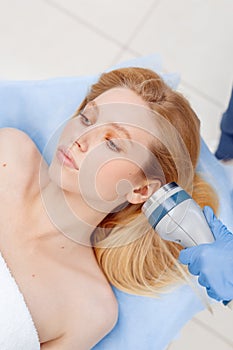 Cosmetology Service. Young woman at beauty clinic lying while doctor using body contouring coolwaves system on face