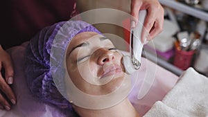 Cosmetology and technology concept - beautician with microdermabrasion device doing face exfoliation to young woman