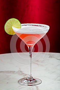 cosmopolitan cocktail with lime and salted rim on marble table and red curtain behind