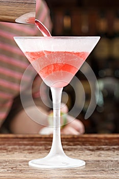 Cosmopolitan cocktail is poured into a glass from a shaker