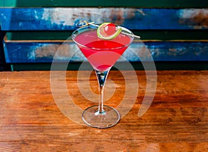 cosmopolitan cocktail served in glass topping with lime slice and cranberry isolated on wooden table side view of hong kong drink