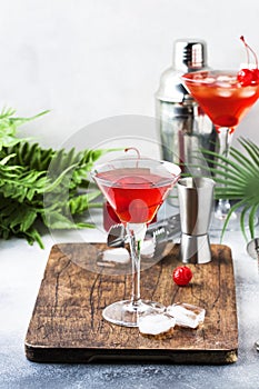 Cosmopolitan cocktail with vodka, liqueur, cranberry juice, lime, ice and orange zest, gray bar counter background, bartender