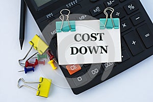 COST DOWN - words on a white sheet with clips on a white background with a calculator, buttons and yellow stationery clips