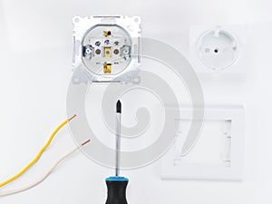 The cost of electrical work and repair. A disassembled socket is next to a screwdriver on a white background.