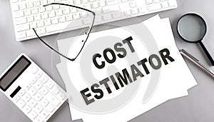 COST ESTIMATOR text on paper with keyboard, calculator on grey background