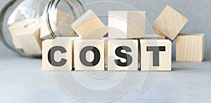 Cost, expense or company profit and loss concept, cube wooden block with alphabet combine word COST on white grid paper