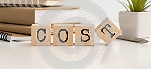Cost, expense or company profit and loss concept, cube wooden blocks with alphabet combine word COST on office desk