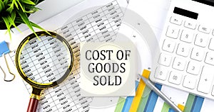 Cost of Goods Sold text on sticker on diagram with magnifier and calculator. Business concept