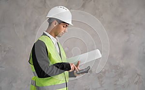 The cost of a new home. Muslim young man with drawings and a calculator  on grey background. Estimate of