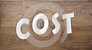 Cost word letters cut from white paper on wooden background. Cost, expense or company profit and loss business concept, analyze