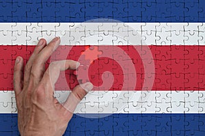 Costa Rica flag is depicted on a puzzle, which the man`s hand completes to fold