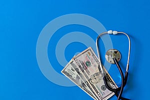 Costly treatment. Stethoscope and dollars on blue background
