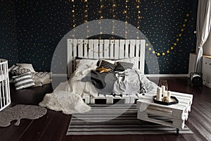 Cosy bedroom interior with a white wooden bed, flashlights, candles and dark walls. Christmas decoration concept.