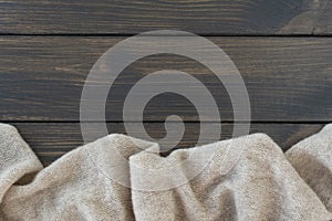 Cosy beige warm wool plaid lie on dark wooden background.