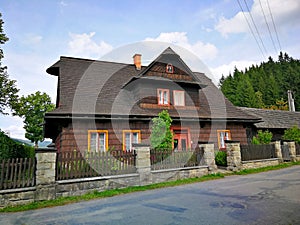 Cottage built entirely of wood, with wooden fence, standing by the asphalt road