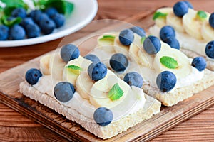 Cottage cheese, bananas and berries sandwiches. Diet sandwiches with crispbread on wooden board. Closeup