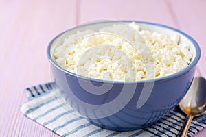 Cottage cheese in blue bowl on purple wooden background