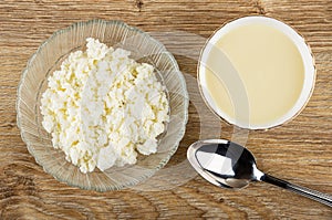 Cottage cheese in bowl, bowl with condensed milk, spoon on wooden table. Top view