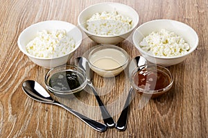 Cottage cheese, bowls with gooseberry jam, condensed milk, boiled condensed milk, spoons on table