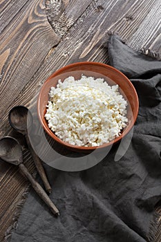 Cottage cheese in a ceramic bowl, wooden spoons, napkin on a wooden brown table.