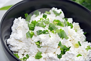 Cottage cheese with chives in black ceramic bowl on rustic woode