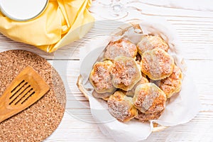 Cottage cheese cookies sprinkled with sugar in a basket and a cup of milk on a wooden table