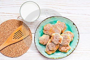 Cottage cheese cookies sprinkled with sugar on a plate and a cup of milk on a wooden table