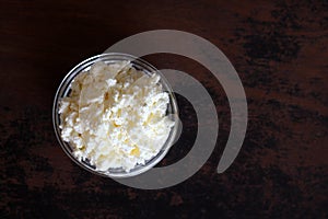 Cottage cheese crumbly in a glass bowl on a wooden old brown tabletop top view