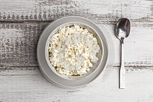 Cottage cheese or curd in bowl and spoon on white wooden rustic table. Healthy organic, diet and farm food