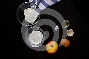 Cottage cheese, flour, apple, egg, oil, salt on a dark background