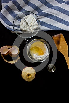 Cottage cheese, flour and eggs, oil, apple on a dark background