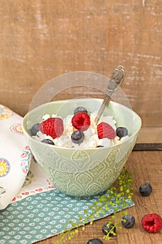 Cottage cheese with fresh raspberries and blueberries in a bowl for healthy breakfast with ripe berries over rustic wooden